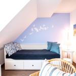 Schlafzimmer mit Dachschrägen, Bett mit Kissen und Wanddekoration.