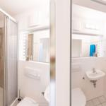 Badezimmer mit Dusche, Waschbecken und Toilette. Spiegel und blaue Handtücher sichtbar.