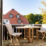 Terrasse mit Tisch und zwei Stühlen, Blick auf ein Haus mit rotem Dach.