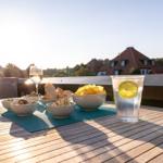Auf der Terrasse steht ein Tisch mit Speisen und Getränken. Im Hintergrund sind Häuser und Bäume zu sehen.