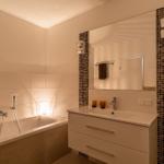 Badezimmer mit Badewanne, Waschtisch und Spiegel mit Mosaikverkleidung.