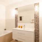 Badezimmer mit Badewanne, Waschtisch und Spiegel mit Mosaikrahmen.