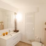Badezimmer mit Waschbecken, Spiegel, Heizkörper und Toilette.