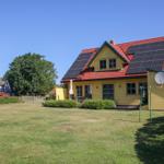 Gelbes Haus mit rotem Dach und Solarpaneelen. Garten mit Rasen und Sträuchern.