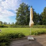 Terrasse mit Sonnenschirm, Blick auf grünen Garten und Bäume.