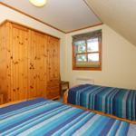 Zimmer mit zwei Betten, Holzschrank und Fenster mit Blick auf Bäume.
