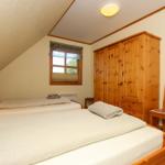 Zwei Betten, Holzschrank und Stuhl im Dachzimmer mit Fenster und Deckenleuchte.