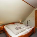 Schlafzimmer mit Holzbett, Nachttisch und Lampen unter schrägem Dach.