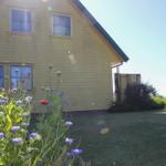 Gelbes Haus mit Garten und Blumen im Vordergrund unter blauem Himmel.