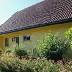 Gelbes Holzhaus mit rotem Dach und grüner Umgebung.