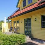 Gelbes Haus mit Terrasse, Tisch, Stühlen und Sonnenschirm. Roter Ziegeldach und grüne Fensterläden.