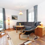 Wohnzimmer mit Sofa, zwei Sesseln, Tisch und Fenstern.