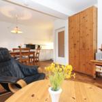 Wohnzimmer mit Essbereich, Holzmöbel und Fernseher. Im Vordergrund eine schwarze Relaxliege.