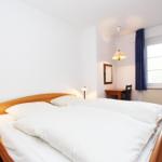 Ein Schlafzimmer mit Doppelbett, Schreibtisch und Fenster mit Vorhängen.