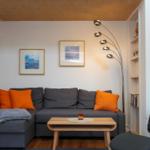 Ein Wohnzimmer mit grauem Sofa, orangefarbenen Kissen und einem Holztisch.