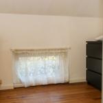 Zimmer mit Holzboden, Fenster mit Vorhang und Schrank.
