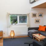Wohnzimmer mit Sofa, Fernseher und Fenster mit Blick auf Grün.