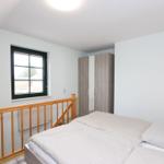 Schlafzimmer mit Doppelbett, Holzgeländer und Fenster mit Blick nach außen.