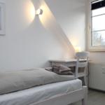 Ein Schlafzimmer mit Bett, Schreibtisch und Fenster. An der Wand hängt ein Bild mit einem Hirsch.