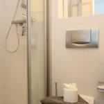 Dusche mit Glaswand, Spiegel, Toilettenpapier und Waschbecken.