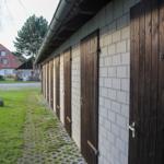 Reihe von Holztüren an einer weißen Ziegelwand mit gepflastertem Weg und Gras.