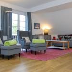 Wohnzimmer mit grauen Sesseln, Sofa und Holzboden. Rote Teppich und Fenster mit Blick.