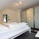 Schlafzimmer mit weißem Bett, Glaswand-Schrank und Dachschrägen.