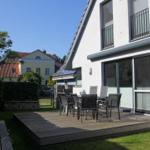 Terrasse mit Sitzgruppe vor modernem Haus mit Garten und Nachbarhaus im Hintergrund.