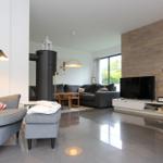 Wohnzimmer mit Sofa, Fernseher und Holzwand. Links Sessel und Stehlampe. Boden glänzend poliert.