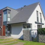 Moderne Villa mit Ziegelfassade und grauem Dach, umgeben von Grünfläche und Steinmauer.