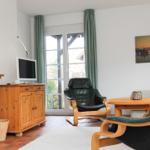 Wohnzimmer mit zwei schwarzen Ledersesseln, Holztisch und TV auf Holzschrank.