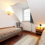 Zwei Betten, ein Fenster, eine Stehlampe und ein Schreibtisch im Dachzimmer.
