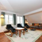 Wohnzimmer mit drei schwarzen Sesseln, Sofa, Tisch und Teppich auf Terrakottboden.