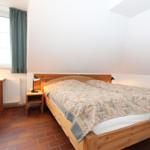 Schlafzimmer mit Holzbett, Schreibtisch und Fenster. Boden aus Terrakottafliesen.
