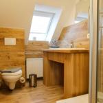 Badezimmer mit Holzwand, Toilette, Waschtisch und Dusche unter Dachschrägen.