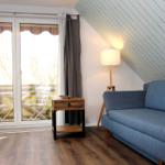 Ein Wohnzimmer mit blauem Sofa, Holzboden und Dachschrägen. Vor dem Fenster befindet sich eine Terrasse.