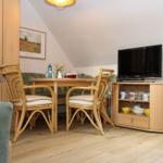 Esszimmer mit Holztisch, Stühlen und Fernseher. Wandbild und Küchenbereich sichtbar.
