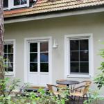 Haus mit Terrasse, Tisch und Stühlen, umgeben von Bäumen und Sträuchern.