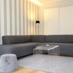 Ein Wohnzimmer mit grauem Sofa, transparentem Tisch und gestreifter Wand.