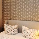 Doppelbett mit floralen Kissen und Tapete mit Muster.