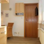 Kleines Zimmer mit Holztür, Schrank, Stuhl und Fenster mit Vorhang.