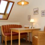 Esstisch mit Bänken und Stuhl unter Dachschräge mit Fenster und Lampe.