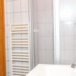 Bad mit Dusche, Waschbecken und Heizkörper an der Wand.