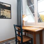 Schreibtisch mit Stuhl unter Fenster, Wandbild und Lampe.