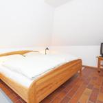 Schlafzimmer mit Holzbett, Nachttisch und Fernseher auf Holzständer.