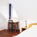 Schlafzimmer mit Bett, Schreibtisch und Fenster unter Dachschräge.