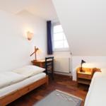 Zwei Betten, Schreibtisch, Fenster und Nachttisch mit Lampe.