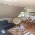 Wohn- und Essbereich mit Sofa, Rattanmöbeln und Holztisch. Wand mit Segelyacht-Motiv.