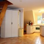 Küche mit Fenster, Holztreppe und Schrank. Fliesenboden und weißer Kühlschrank.