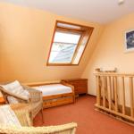 Schlafzimmer mit Dachschräge, Dachfenster, Holzbett und Wicker-Sessel.